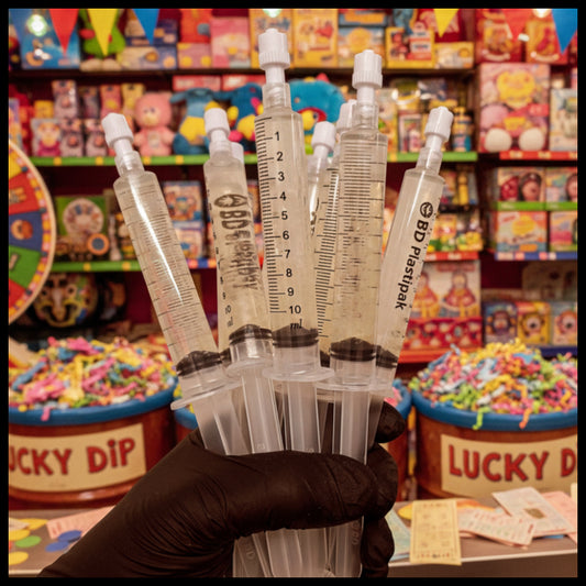 Hand holding multiple syringes with a colorful candy store background